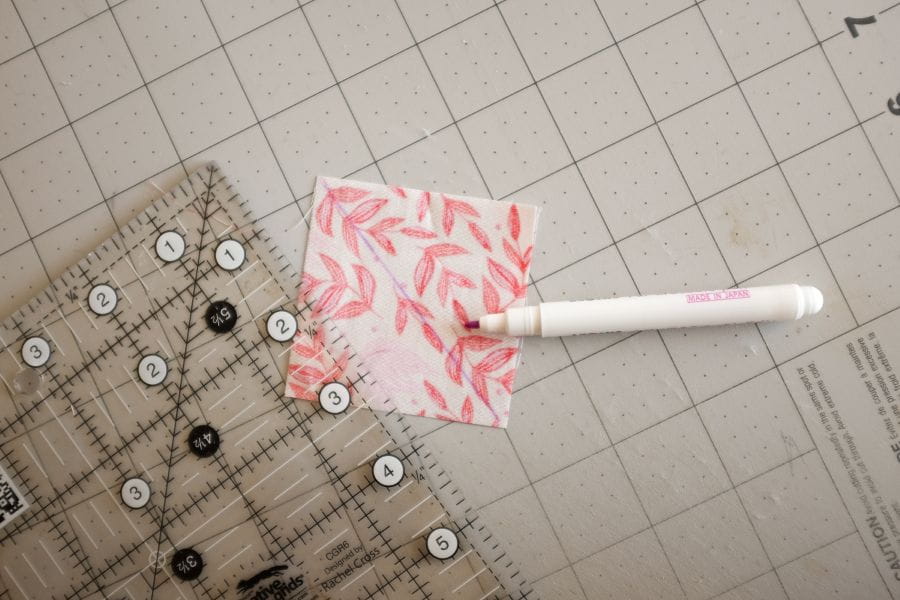 example of quick corner unit with piece of square fabric on quilting mat, with a marker and quilting ruler